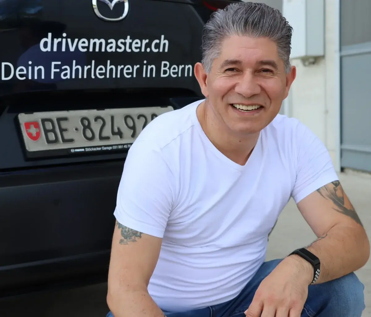 Mishel Memedovski - Fahrlehrer der Drivemaster Fahrschule Bern vor seinem Mazda Fahrschulauto mit drivemaster.ch Beschriftung