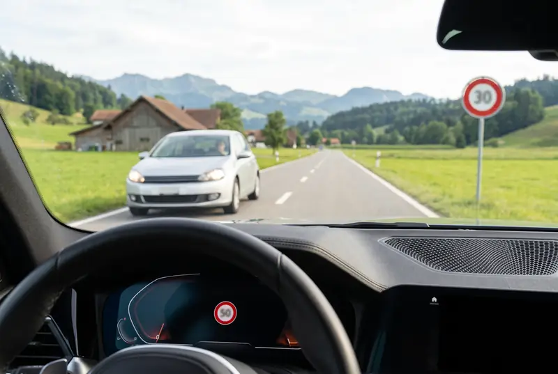 Blick aus dem Auto auf eine Schweizer Landstrasse: Am rechten Rand steht ein Signal mit Höchstgeschwindigkeit 30, die Verkehrszeichenerkennung im Display zeigt 50 an